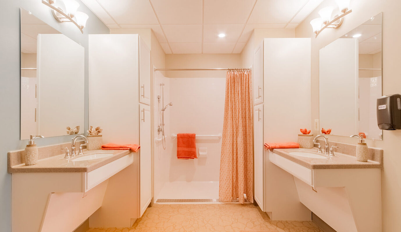 Decorated bathroom with two sinks, walk in shower, and tall cabinets