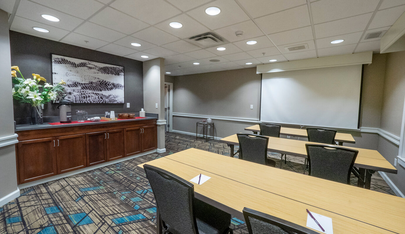 Small room with video projector screen, three tables with 2 chairs at each table, and coffee station on countertop at Residence Inn in Hazelton, PA