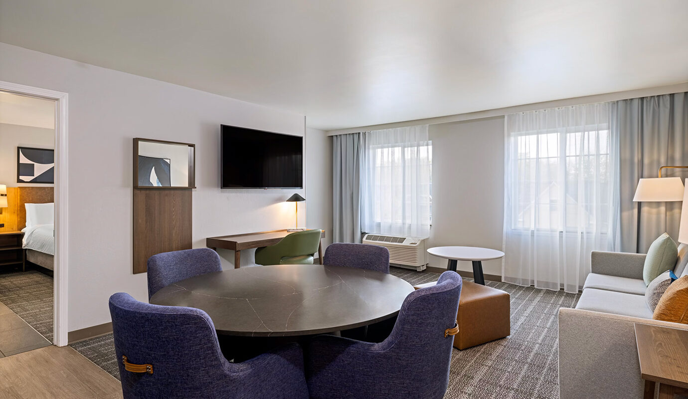 Guest room with bed, table and chairs, tv on wall, desk, and couch