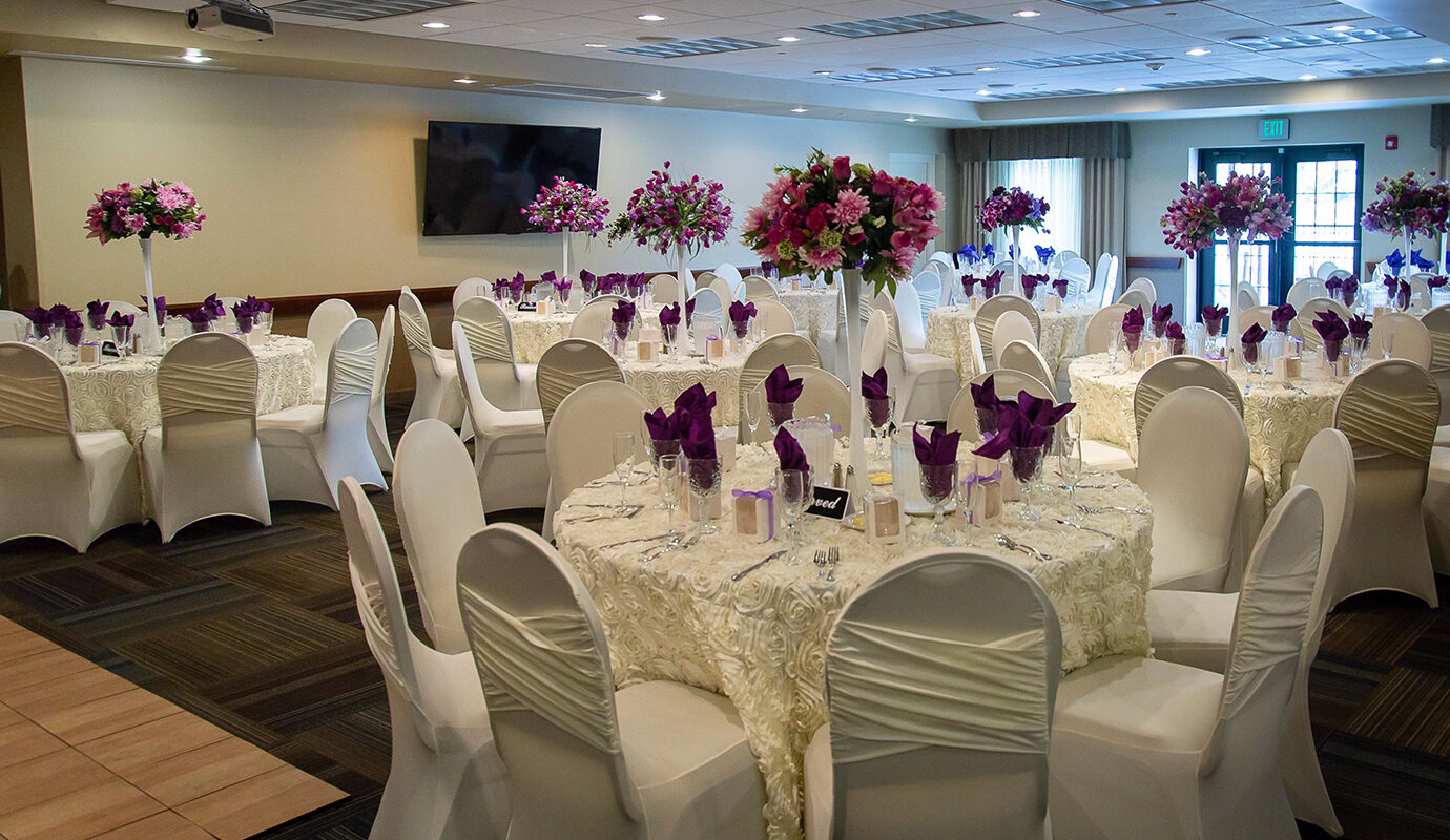 Banquet hall decorated for a wedding with white and cream linens and purple flowers