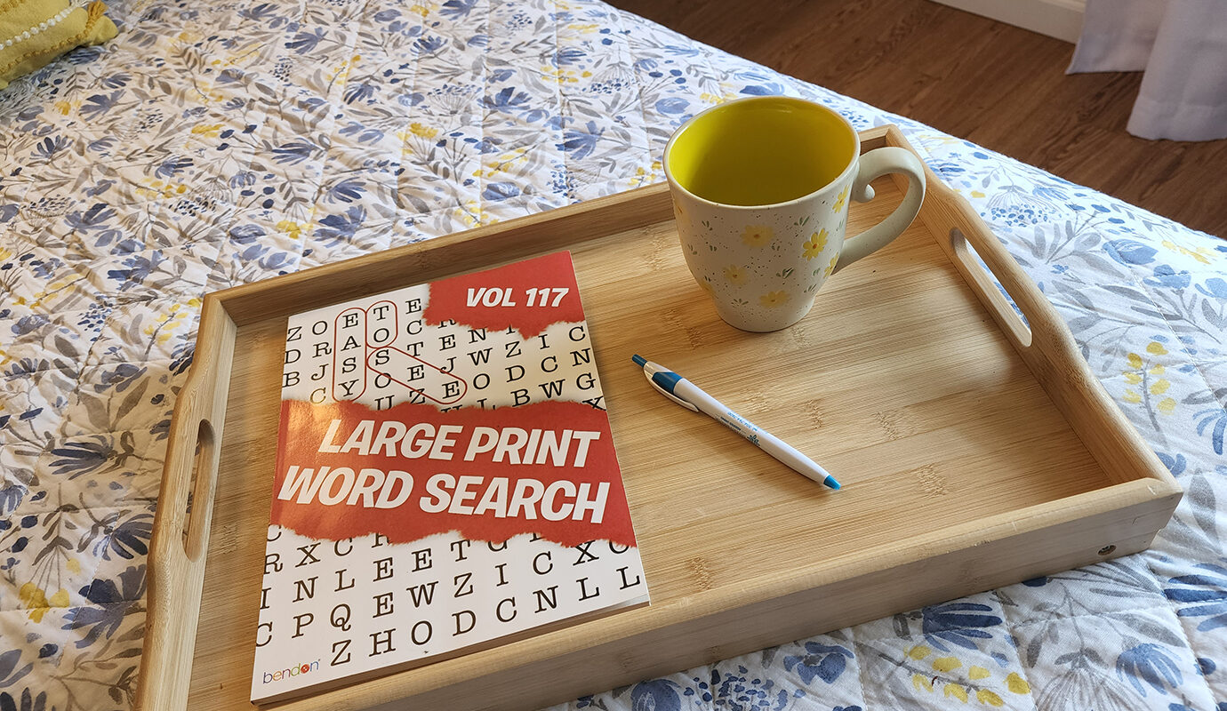 Tray with crossword puzzle and mug on bed